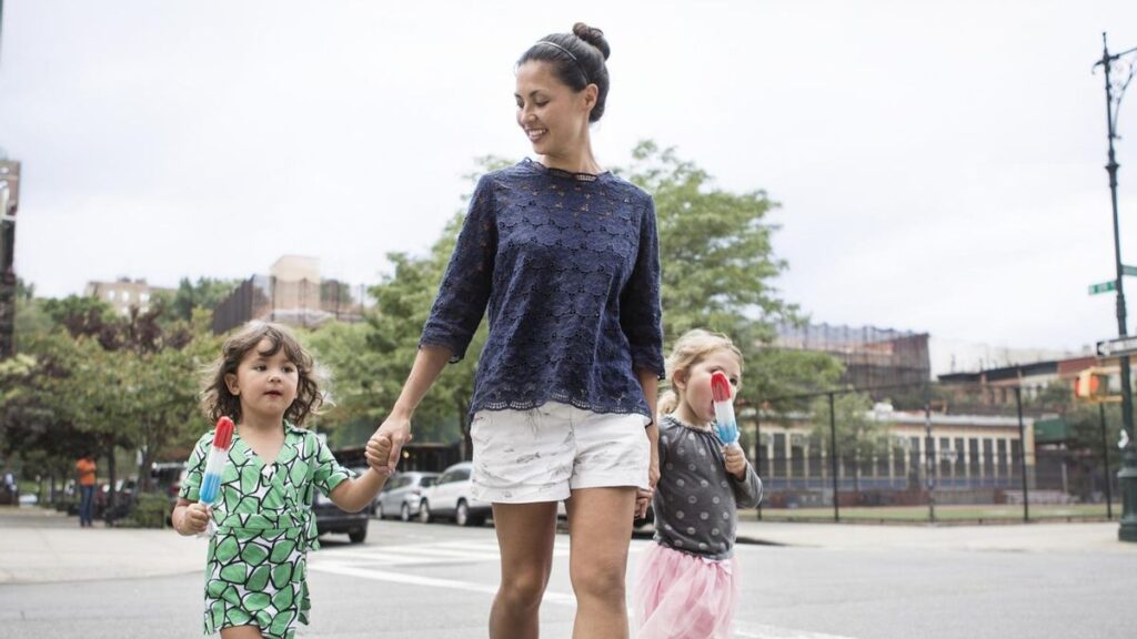 Girls eating ice creams while walking with mother on street