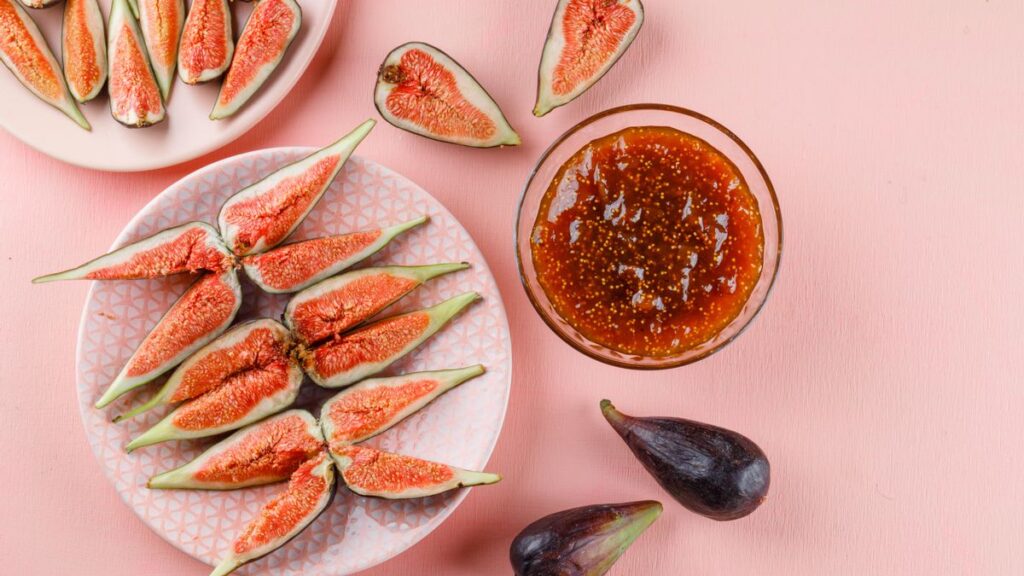Figs with fig jam in plates on pink background, flat lay.