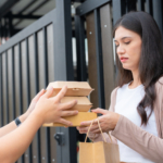 Packages are being delivered by a delivery man to a female customer at her door. Smiling, the young lady signs the receipt document.