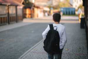Back view of boy in white shirt with black backpack go home after the lesson